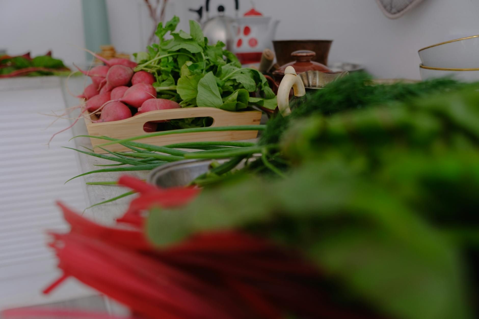 A variety of fresh vegetables including radishes and greens laid out on a kitchen countertop.
