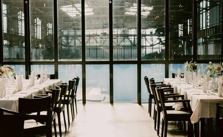 Elegant dining setup in an industrial venue with large windows and floral decor.
