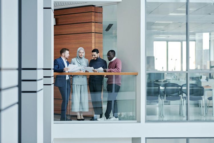 Group of diverse colleagues collaborating in a modern office with glass walls, emphasizing teamwork and inclusivity.