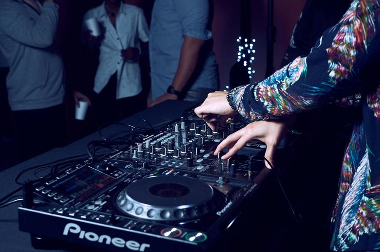 Hands of DJ adjusting audio mixer at a vibrant nightclub party.