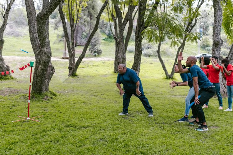 A diverse group of adults participates in a team building game outdoors in a park.