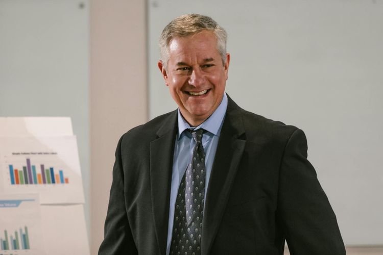 Smiling businessman in a corporate setting with charts. Professional and confident.
