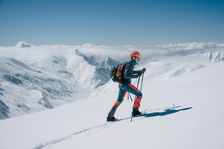 An adventurous skier scaling a snowy mountain peak under a clear blue sky.