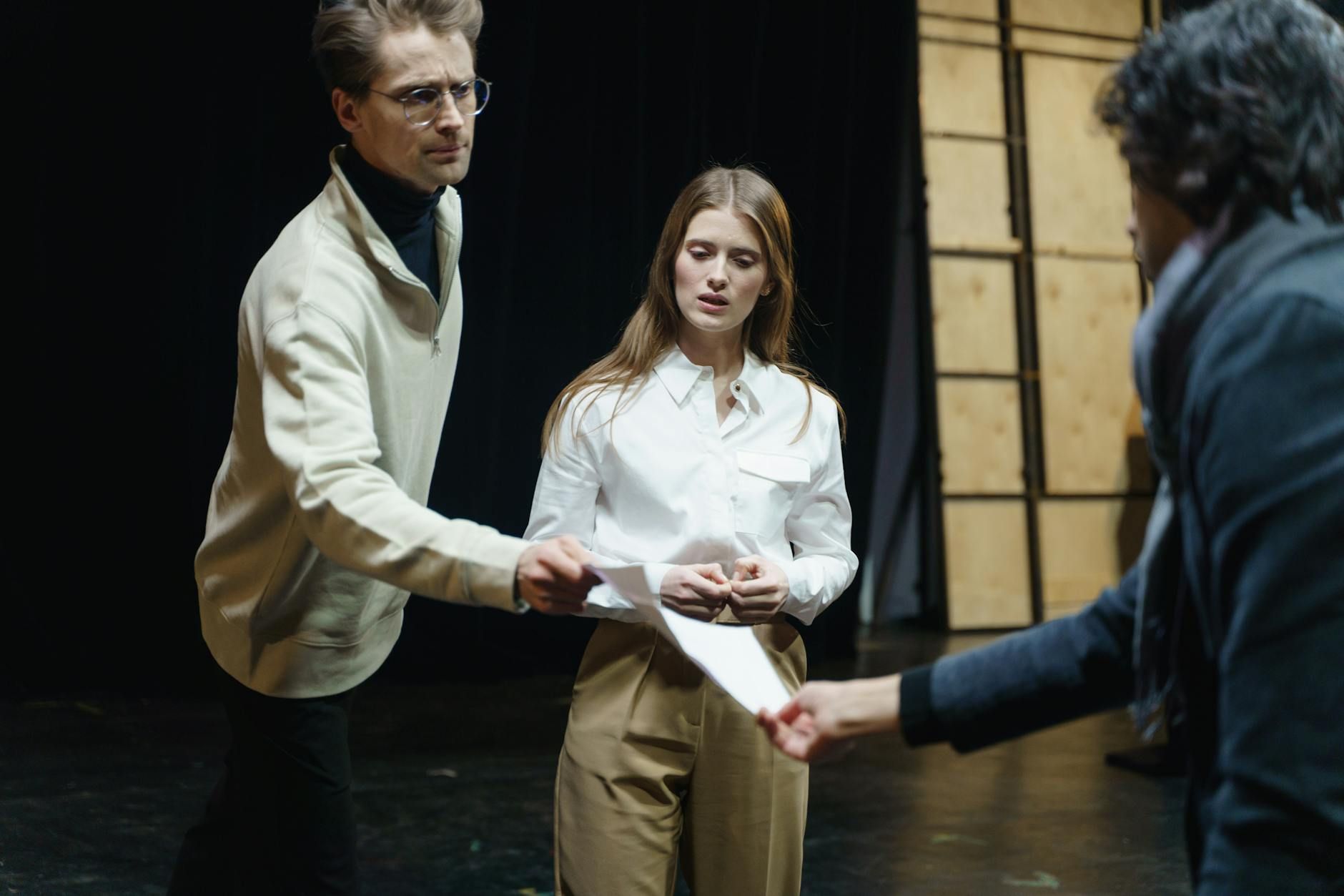 Actors engage in a rehearsal, exchanging scripts on stage, embodying theatrical drama and emotion.