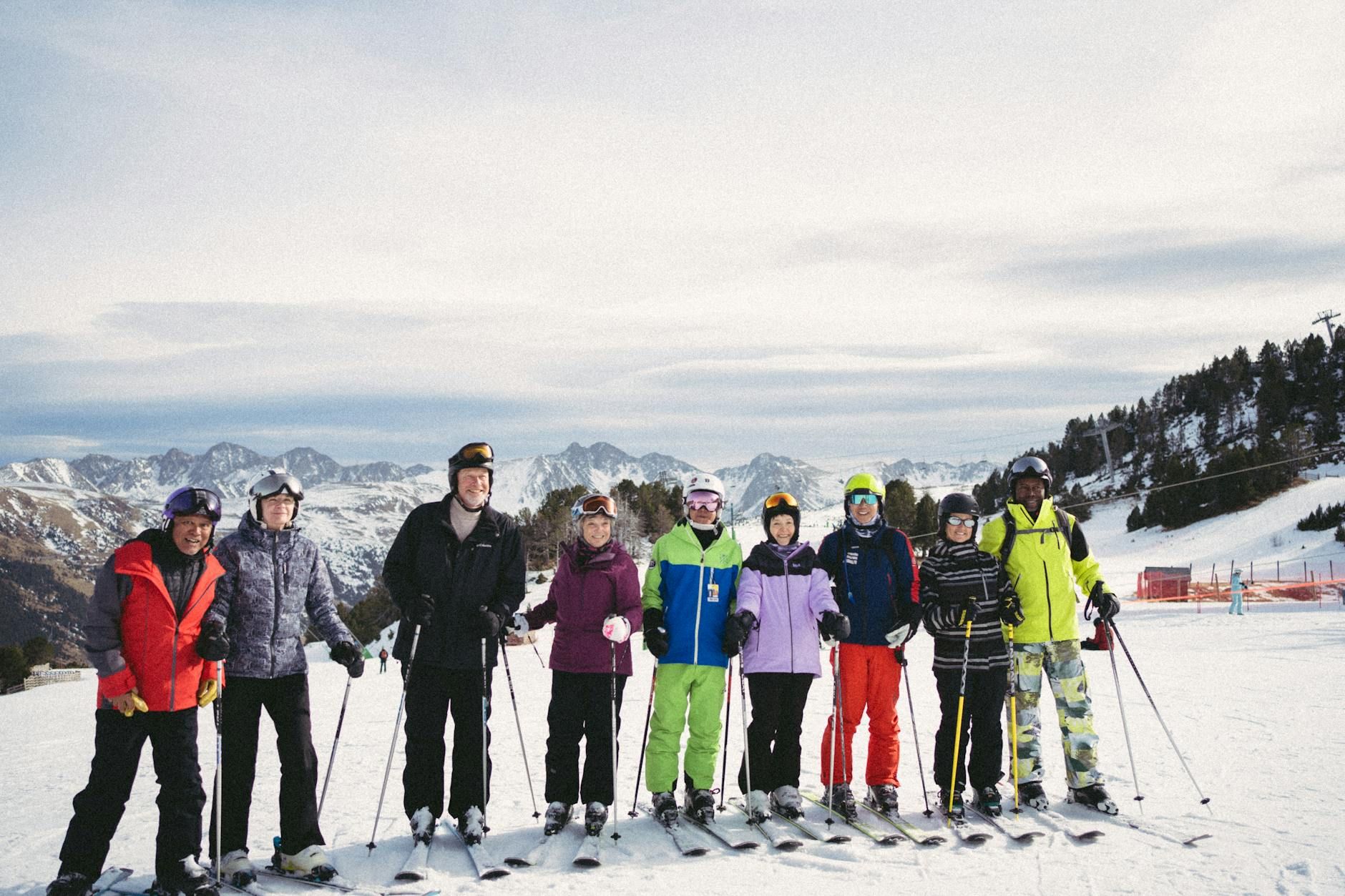 A diverse group of skiers posing on a ski slope against a snowy mountain backdrop. A diverse group of skiers posing on a ski slope against a snowy mountain backdrop.