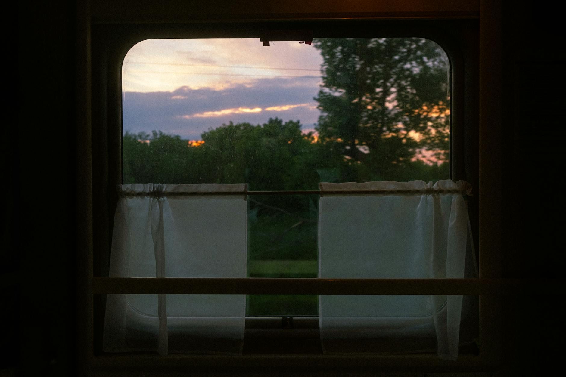 View through a vintage train window capturing a serene sunset and landscape. View through a vintage train window capturing a serene sunset and landscape.