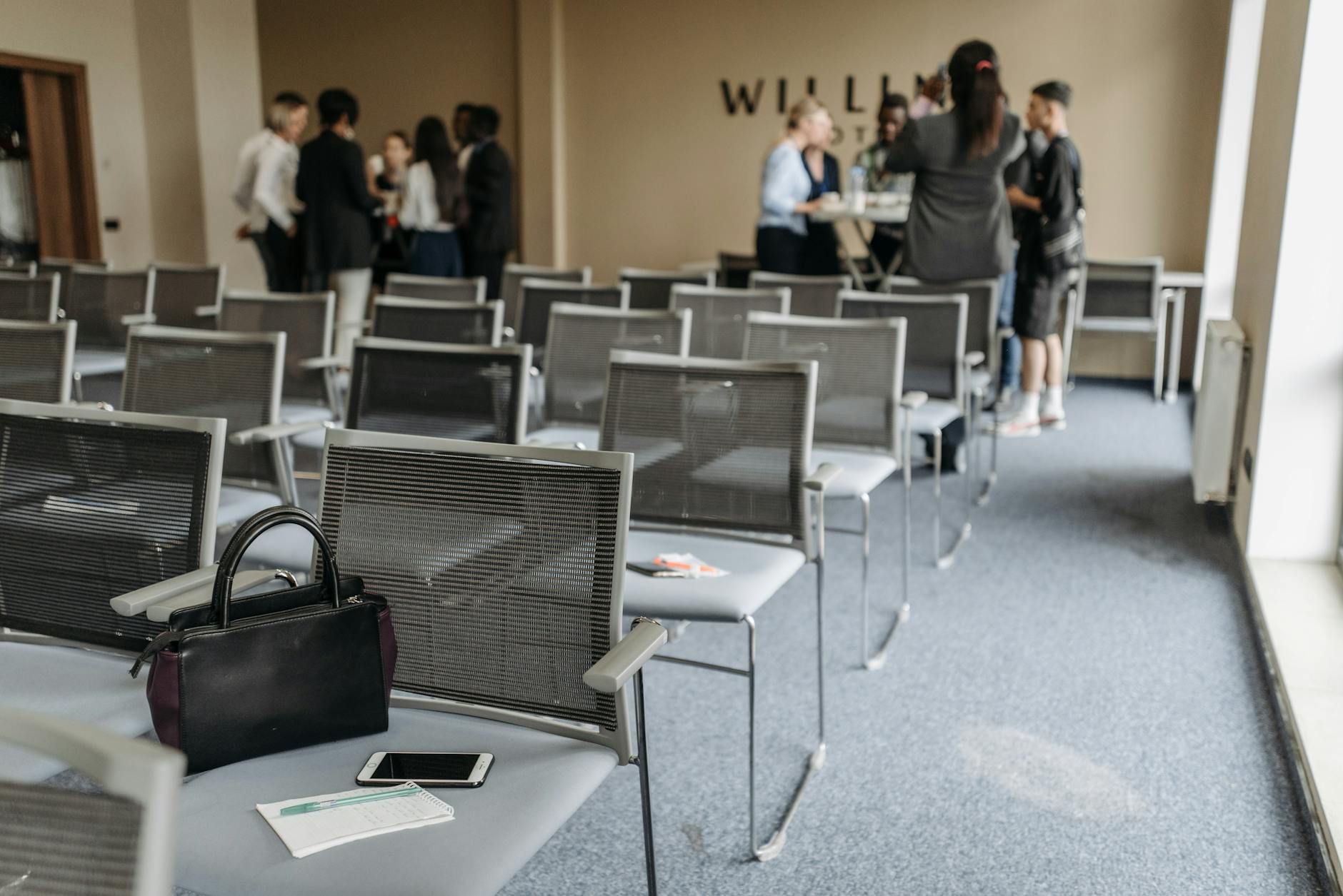 An empty conference room with chairs and a group of people gathered at the back. An empty conference room with chairs and a group of people gathered at the back.
