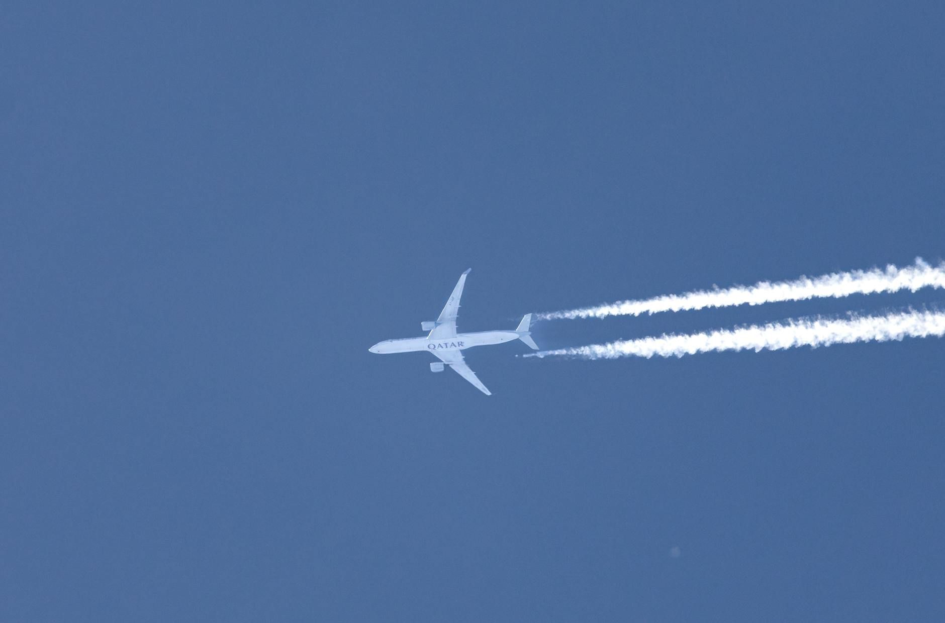 A high-flying Qatar Airways jet leaves contrails in a clear blue sky, showcasing aviation dynamics.