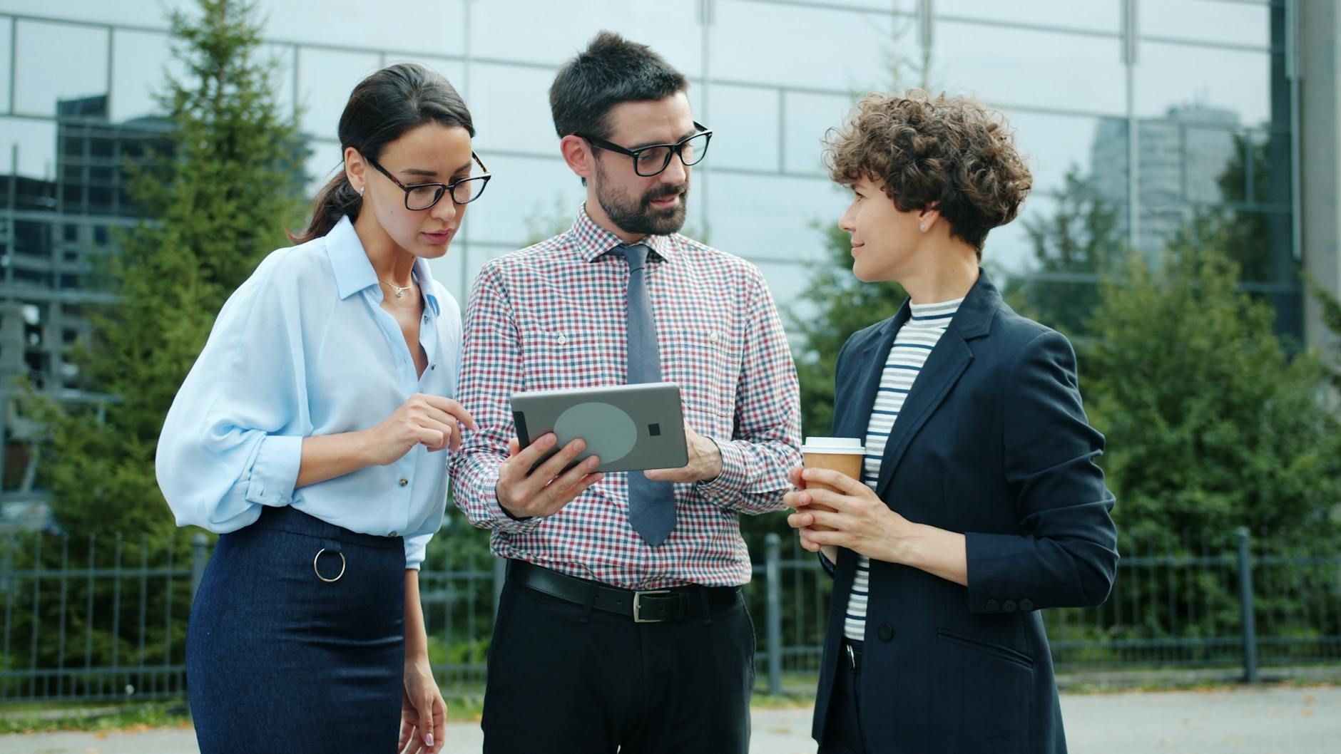 Three colleagues discussing a project using a tablet outdoors
