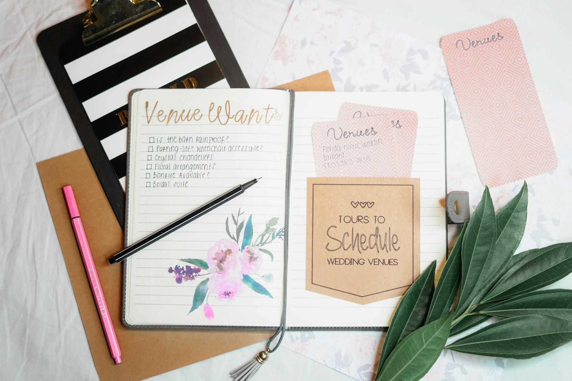 Flat lay of wedding planning materials including a journal, leaves, and stationery. Flat lay of wedding planning materials including a journal, leaves, and stationery.