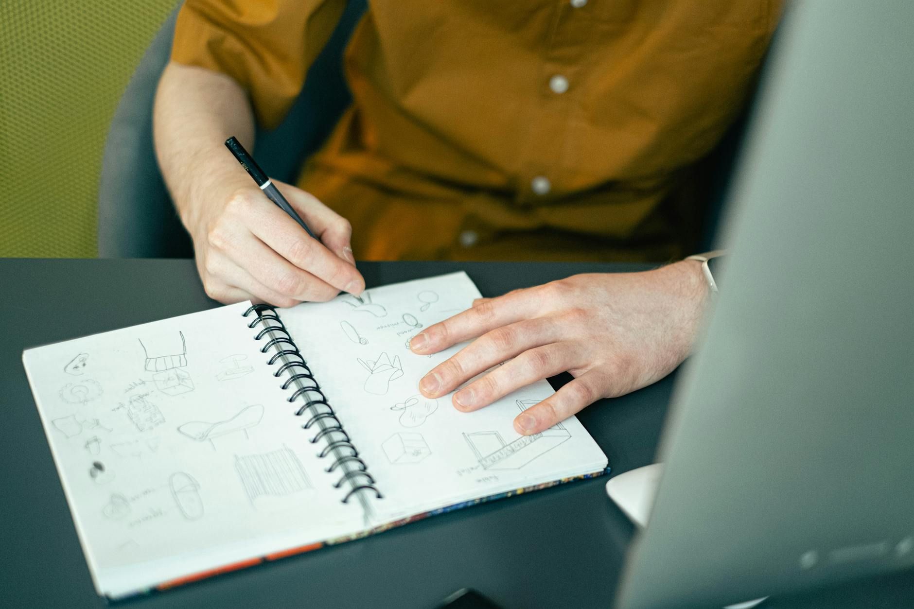 Close-up of a designer sketching ideas in a spiral notebook at a desk, highlighting creativity. Close-up of a designer sketching ideas in a spiral notebook at a desk, highlighting creativity.