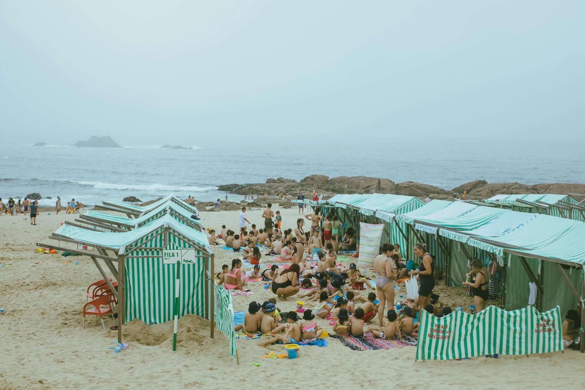 Día de verano en la playa con personas relajándose y carpas a rayas alineadas en la orilla.